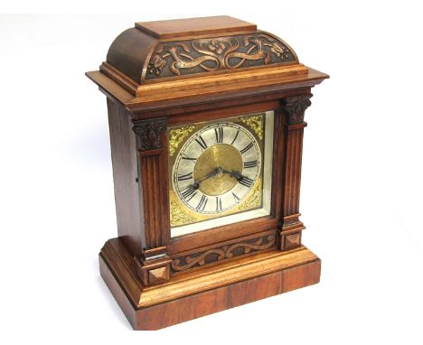 A late 19th Century walnut bracket clock of stepped architectural form with reeded columns flanking door and carved Art Nouve