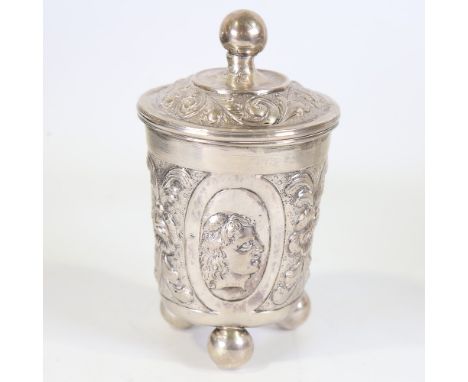 A German silver beaker and cover, Hanau, relief embossed figural and foliate decoration on three bun feet, by Neresheimer wit