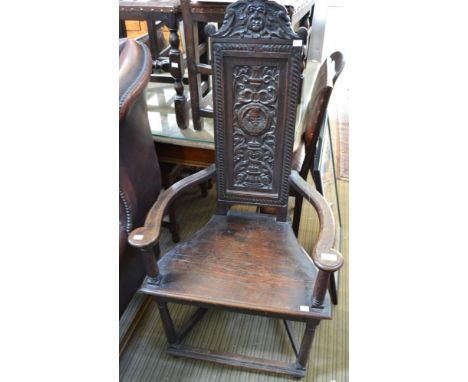 An oak chair, the carved back with Green Man crest and the image of an Elizabethan gentleman, open arm, plank seat