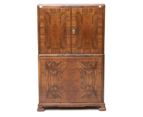 An Art Deco Figured Walnut Tallboy, the top section with two doors enclosing a shelf, the base with four graduating drawers, 