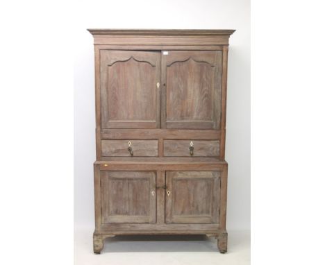 George III limed oak livery cupboard with concave cornice and enclosed by pair of arched panelled doors, with faux drawers an