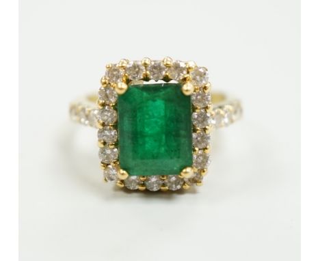 A modern 18ct gold and single stone emerald set dress ring, with diamond set border and shoulders, size L, gross weight 6.5 g