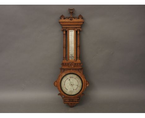 A Victorian honey oak barometer, with silvered dial surmounted by thermometer, within a leaf carved case