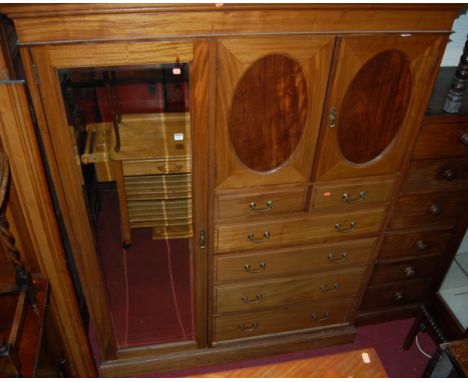 *An Edwardian mahogany gentleman's wardrobe having single bevelled mirrored long door, twin oval recess panelled upper cupboa