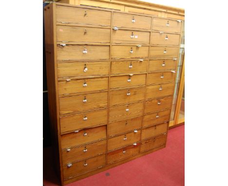 A large circa 1900 pitched pine haberdashery cabinet, having upper and lower hinged fall front compartments and six central d