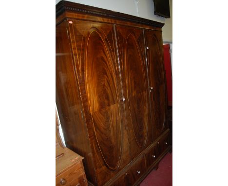 An Edwardian mahogany and flame mahogany three door wardrobe, having interior hanging compartment, fitted linen slides over t
