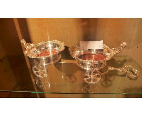 A silver plated twin wine coaster in the form of cherubs on a cart 