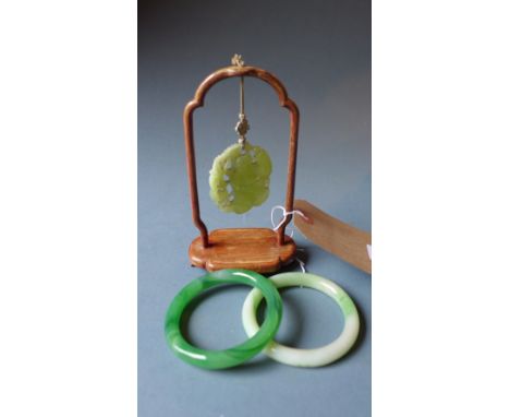A Chinese Jade pendant, carved with a figure, on a wooden stand together with two jade style bangles