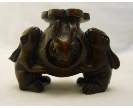 A Japanese carved and stained wood netsuke, worked as a pair of rabbits holding a further rabbit emerging from a gourd