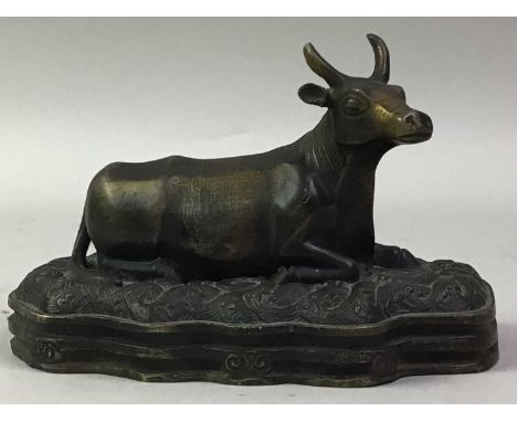 CHINESE BRONZED METAL FIGURE OF A RECUMBENT BULL, on a shaped oval base cast in relief, scroll and crashing wave designs, the