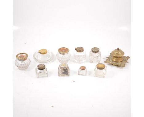 Ten glass inkwells with brass and metal mounts, a brass inkwell with hinged cover on a 10cm square integral stand with scroll