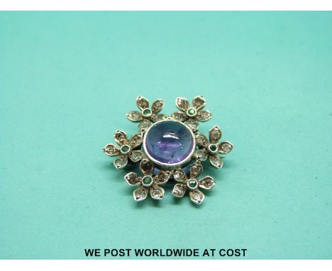 A suffragette brooch set with an amethyst cabochon surrounded by diamonds and emeralds in the form of flowers. 