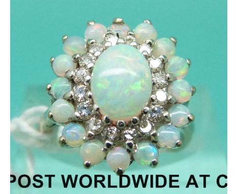 An 18ct white gold ring set with an oval opal cabochon surrounded by a circle of diamonds then a further circle of opals, wit