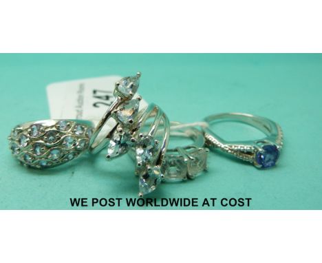 Four silver rings including one set with three square cubic zirconia, one set with blue topaz, and another with amethyst and 