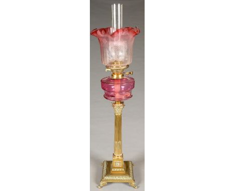 AN EDWARDIAN BRASS COLUMNAR OIL LAMP, WITH CRANBERRY GLASS FOUNT, BRASS BURNER ON STOP FLUTED CORINTHIAN COLUMN, SQUARE BASE 