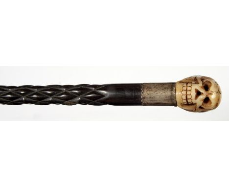 A SPIRALLY CARVED EBONY WALKING CANE WITH CARVED BONE HUMAN SKULL POMMEL AND SILVERED METAL MOUNT, BRASS TIP, 79.5CM Conditio