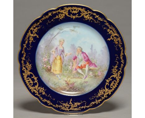 A SEVRES STYLE COBALT GROUND PLATE, C1900, PAINTED WITH 18TH C LOVERS, INDISTINCTLY SIGNED, IN RAISED GILT BORDER AND LOBED R
