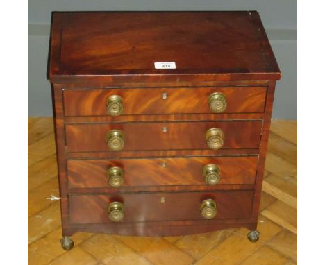 A George IV ebony strung miniature commode chest, of four long drawers with decorative brass knob handles, raised on brass ba