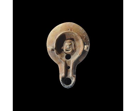 2nd-3rd century AD. A terracotta oil lamp with lugs to the shoulders, long nozzle with raised rim and ring to the discus, fac
