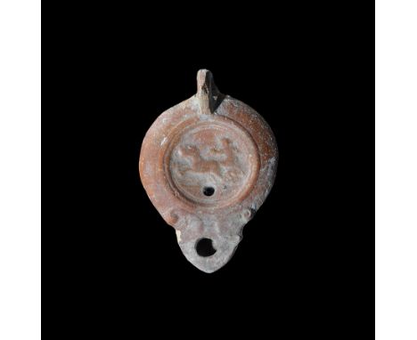 2nd century AD. A terracotta lamp with short nozzle, scrolled shoulders, loop handle to the rear, recessed discus with low-re
