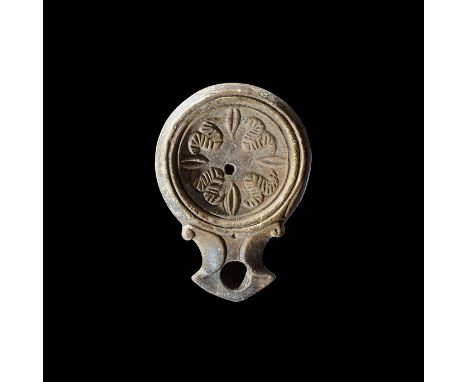 1st century AD. A small terracotta oil lamp with chamfered shoulder, broad nozzle with lateral scrolls, concentric rings to t