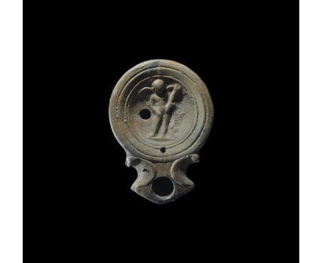1st century AD. A terracotta lamp with deep body, broad nozzle with scrolled shoulders, concentric rings with high-relief fig
