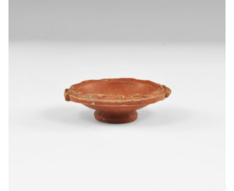 2nd century AD. A small terracotta dish with flared foot, shallow bowl, laurel leaves to the curved rim, imitation strap hand
