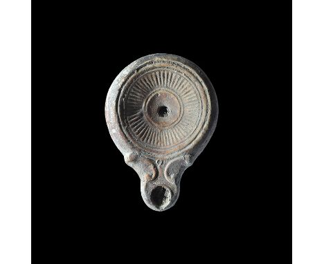 2nd century AD. A terracotta oil lamp with short nozzle and scrolled shoulders, recessed discus with band of radiating lines 