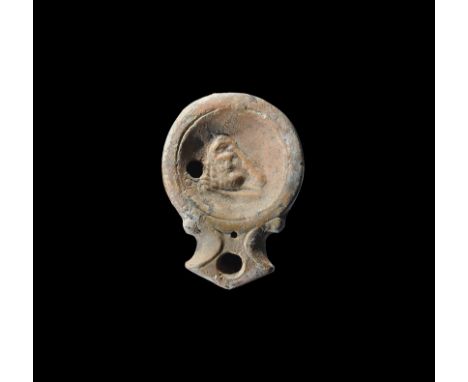 1st century AD. A terracotta oil lamp with broad nozzle, scrolled shoulders, raised ring to the discus, bearded bust of Hercu