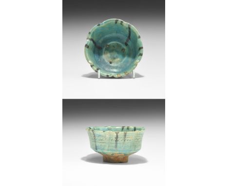 12th-14th century AD. A glazed ceramic footed bowl with flared rim, formed as seven segments with vertical black lines to the