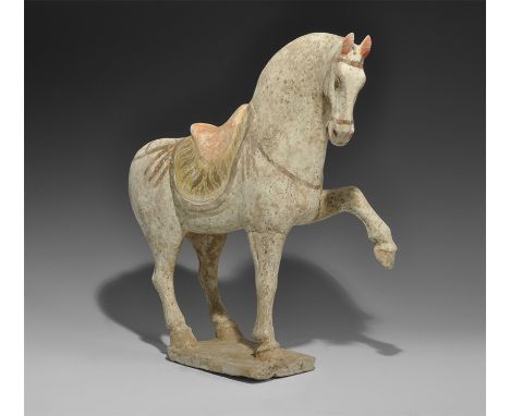 Tang Dynasty, 618-906 AD. A ceramic figurine of a horse with one foreleg raised and arched neck on a rectangular base; finely