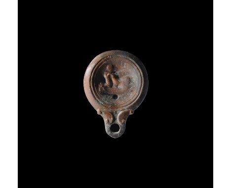 2nd century AD. A discoid terracotta lamp with short nozzle and scrolled shoulders, low-relief erotic scene to the discus. Fr