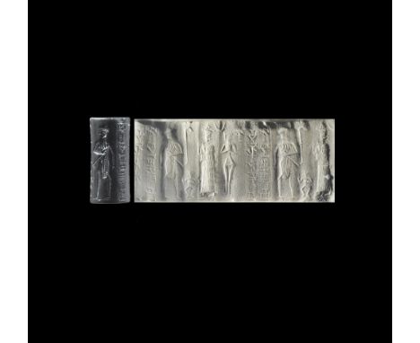 19th-17th century BC. A carved haematite(?) cylinder seal with a bearded king facing a goddess in a flounced robe, smaller fi