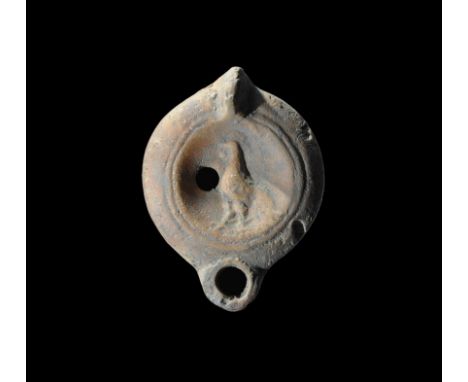 2nd-3rd century AD. A small terracotta oil lamp with lug handle to the rear, short nozzle, flat shoulder, discus with high-re