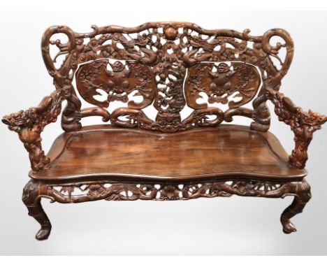 An oriental heavily carved hardwood three seater bench, with carved dragon arm rests, 147 cm long 