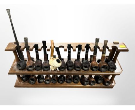 A wooden pipe rack containing 24 various pipes including Meerschaum example with amber stem and bowl in the form of a Sikh.