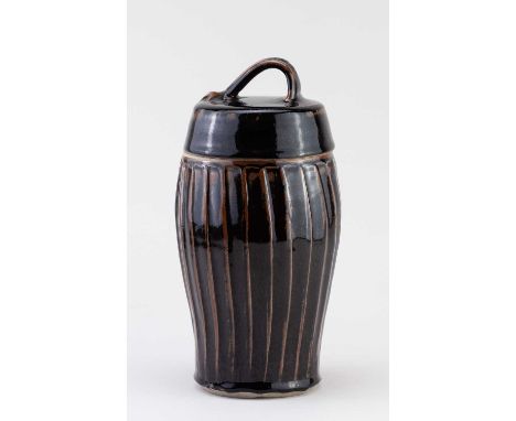 † JEREMY LEACH (born 1941) for Lowerdown Pottery; a tall fluted stoneware jar and cover covered in tenmoku breaking to kaki g