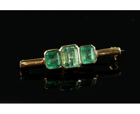 Three stone emerald bar brooch, all rectangular step cut, estimated total weight 3.69 carats, mounted in 18 ct yellow gold, 3