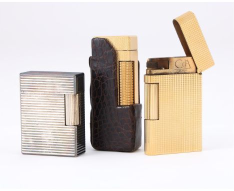 
	
		Y&nbspTHREE LIGHTERS
		To include: a gilt metal lighter by Dunhill, with engine turned decoration and a crocodile leathe
