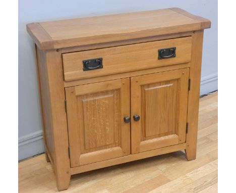 A modern light oak cabinet, comprising of one drawer above two hinged doors, with aged brass handles &amp; knobs, opens to re