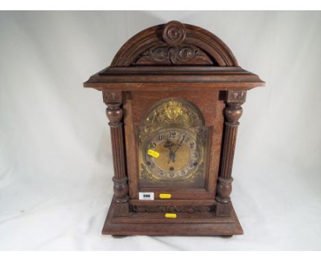 An oak cased bracket style chiming clock, arched brass dial with applied slivered chapter ring and decorative spandrels, thre