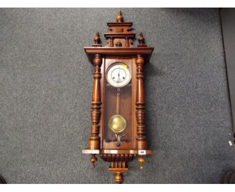 A Vienna style wall clock, walnut case with turned decoration, surmounted by a stepped pediment with applied mask, white enam