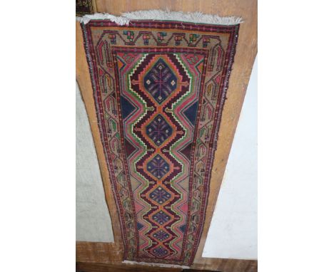 A WOOL RUNNER, the light pink indigo and wine ground with central diamond panels with stylised foliage within a conforming bo