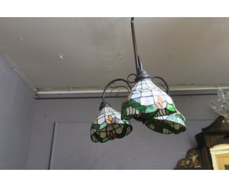 A TIFFANY STYLE BRASS FRAMED THREE ARM CENTRAL LIGHT, the scrolled arms issuing stained glass shades in green white and orang