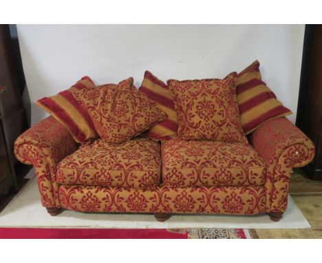 A CONTEMPORARY THREE SEATER SOFA, upholstered in gold and red foliates the rectangular upholstered back above scrolled uphols