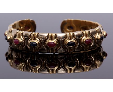 Yellow metal sapphire and ruby set bangle, the stylised design, alternate set with cabochon rubies and sapphires, each in col