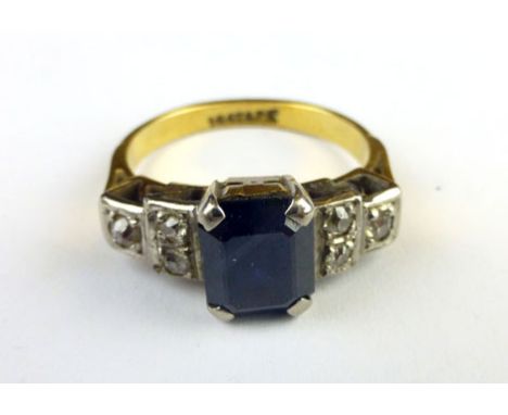 An 18ct yellow gold ring set single step cut dark blue sapphire and having three small diamonds to each shoulder 