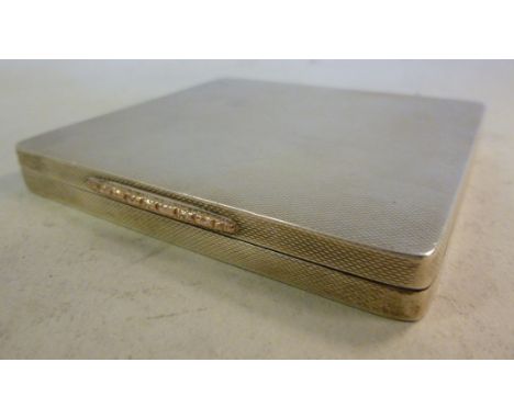 An unfitted silver card case of rectangular form with engine turned decoration and a yellow metal mount on the flush fitting,
