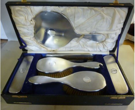 A five piece silver backed dressing table set with engine turned decoration  comprising a hand mirror, a pair of hair brushes