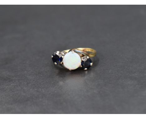 An opal and sapphire trilogy ring, the central circular opal cabochon flanked by two round cut sapphires with cross over shou